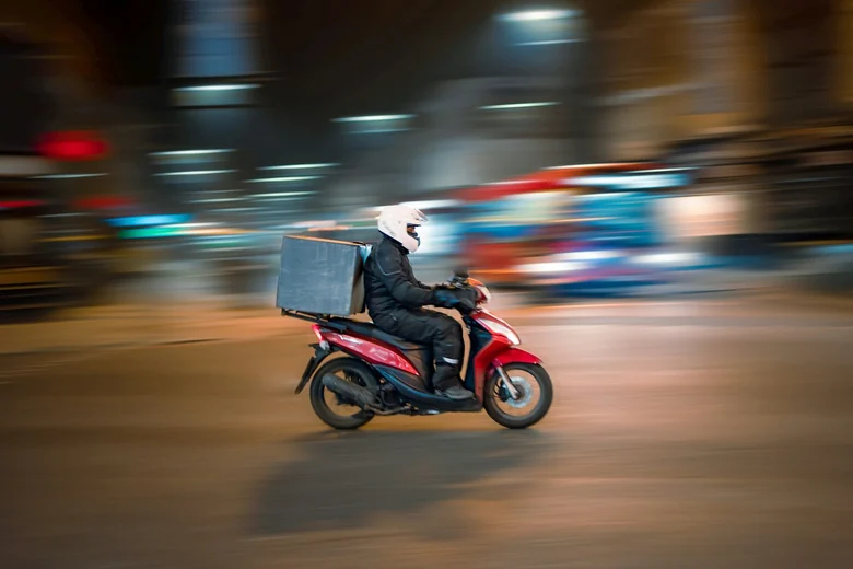 Entregador em scooter vermelha atravessando a cidade
