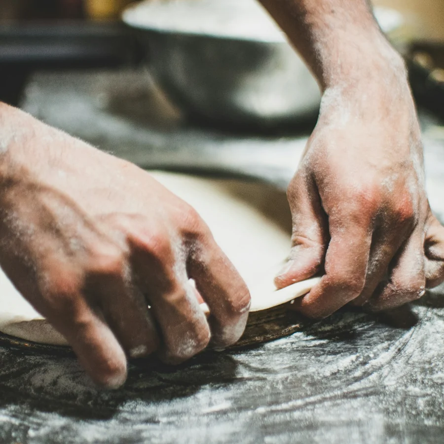 Mãos abrindo a massa de pizza sobre a bancada enfarinhada