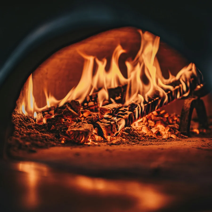 Boca do forno a lenha aceso, com a chama lambendo a parede de tijolo